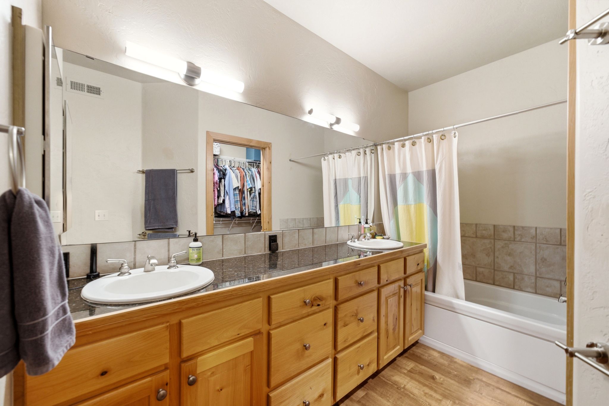 Bathroom featuring a double vanity with light wood cabinetry and stone-finish countertops
