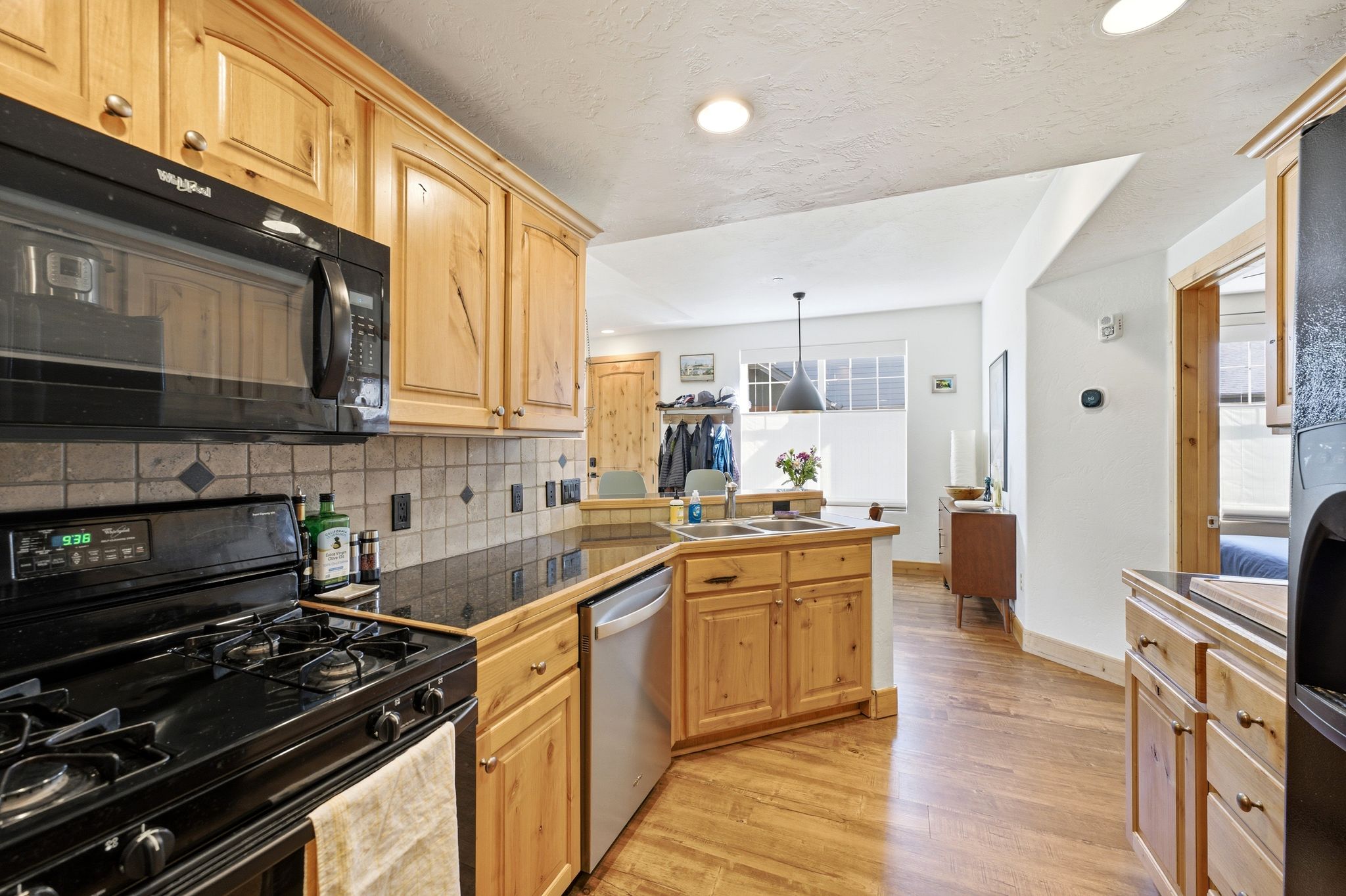 Kitchen featuring wood cabinetry, black countertops, a tile backsplash, and wood-finish flooring