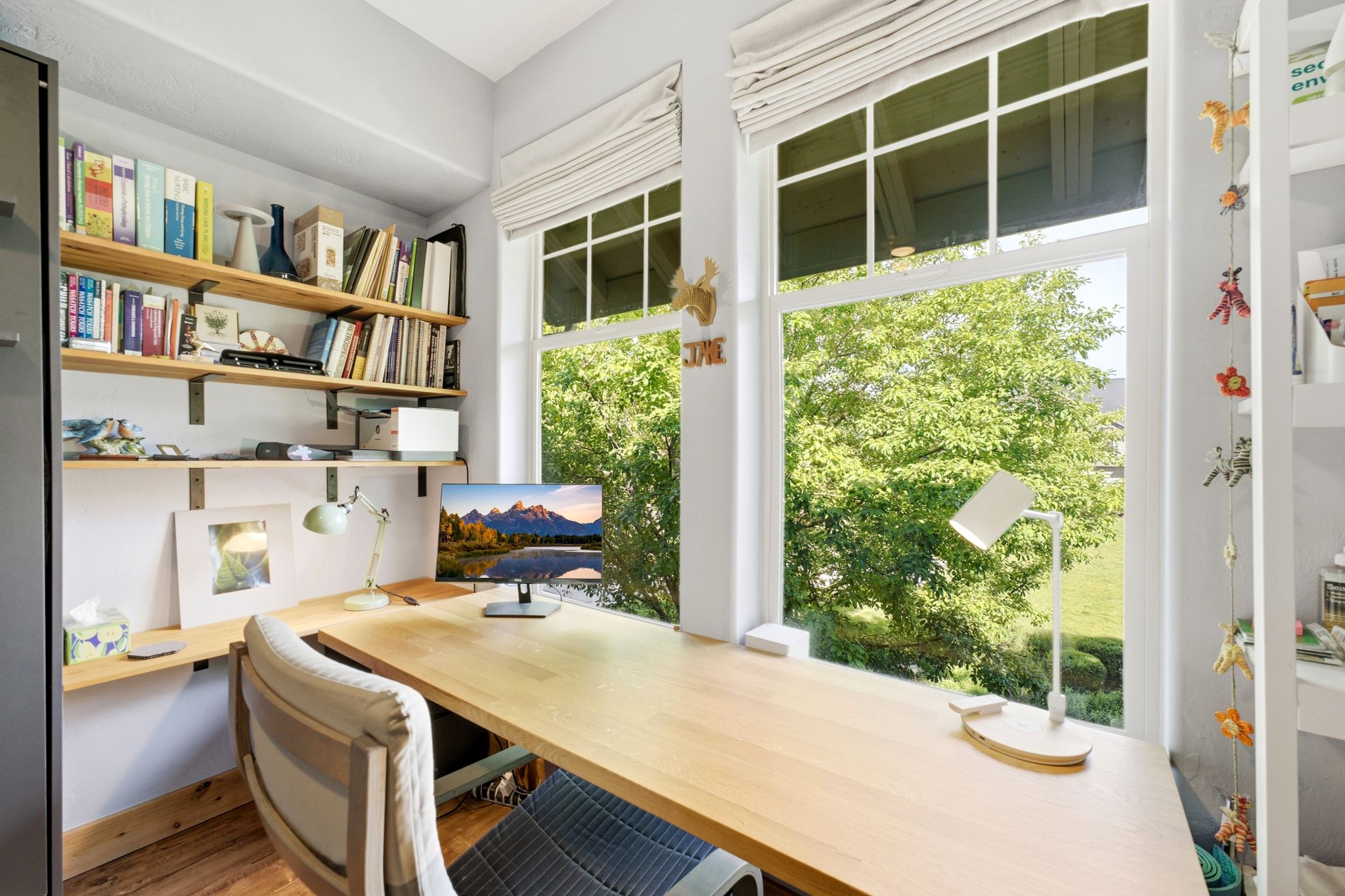 Dedicated workspace featuring a built-in wood-finish desk, dual large windows with white trim, and integrated wall shelving