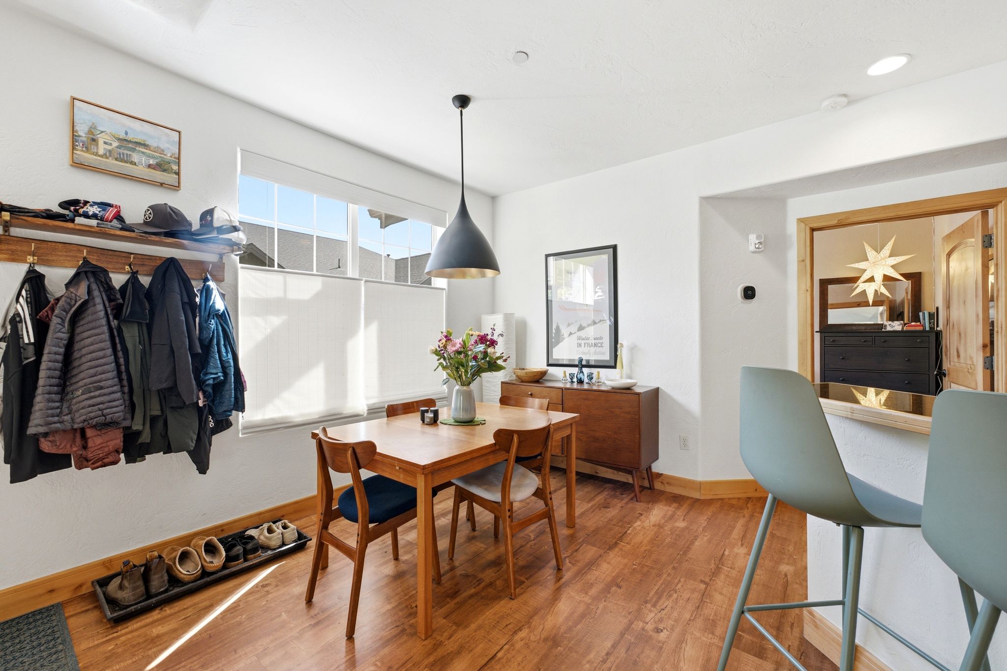 Dining area featuring wood-finish flooring, a contemporary pendant light fixture, and a large window with cellular shades