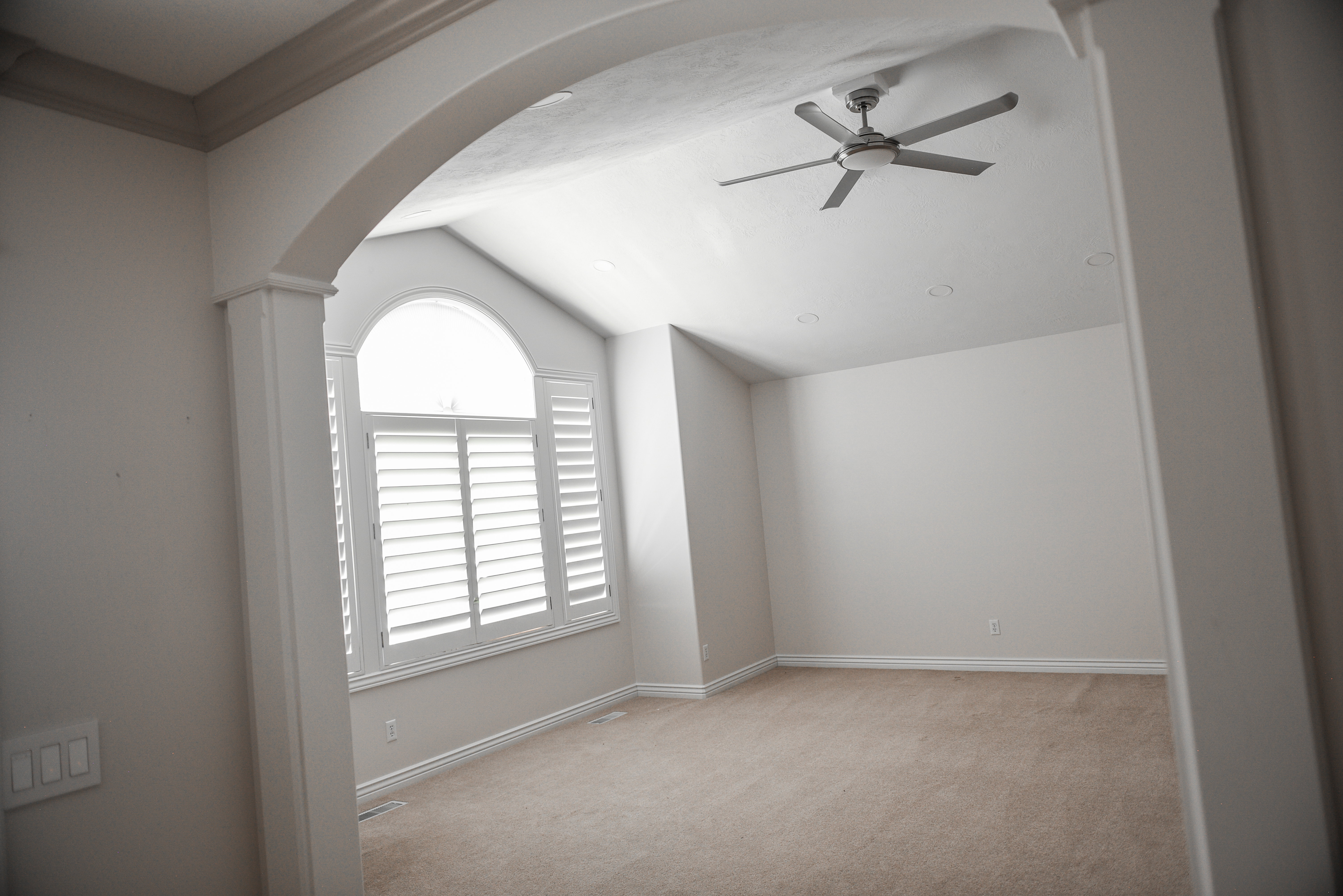 Vaulted ceiling room featuring a large arched window with plantation shutters, ceiling fan, recessed lighting, and neutral carpet flooring
