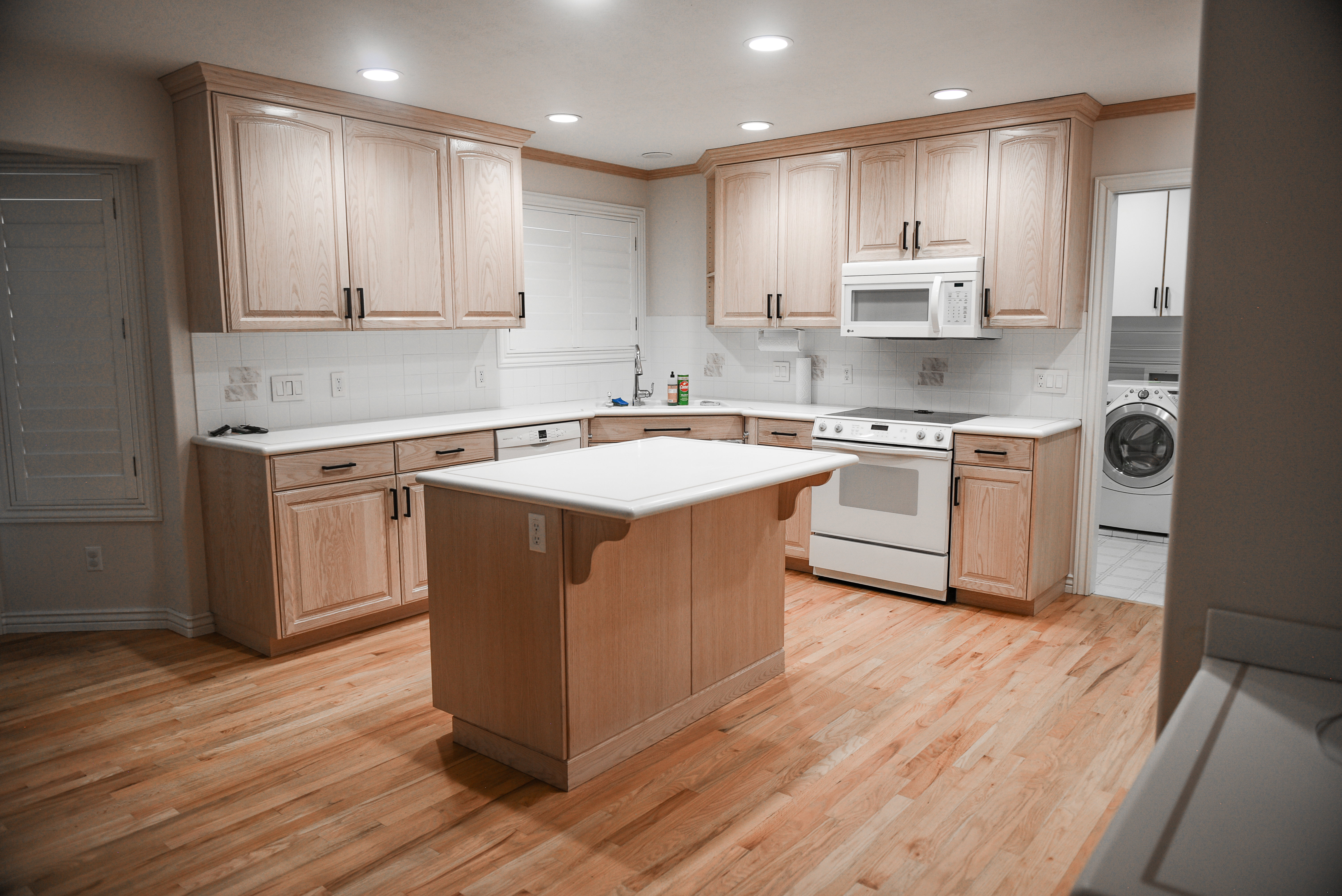 Kitchen featuring an island, wood-finish flooring, light wood cabinetry, white countertops, and a white subway tile backsplash