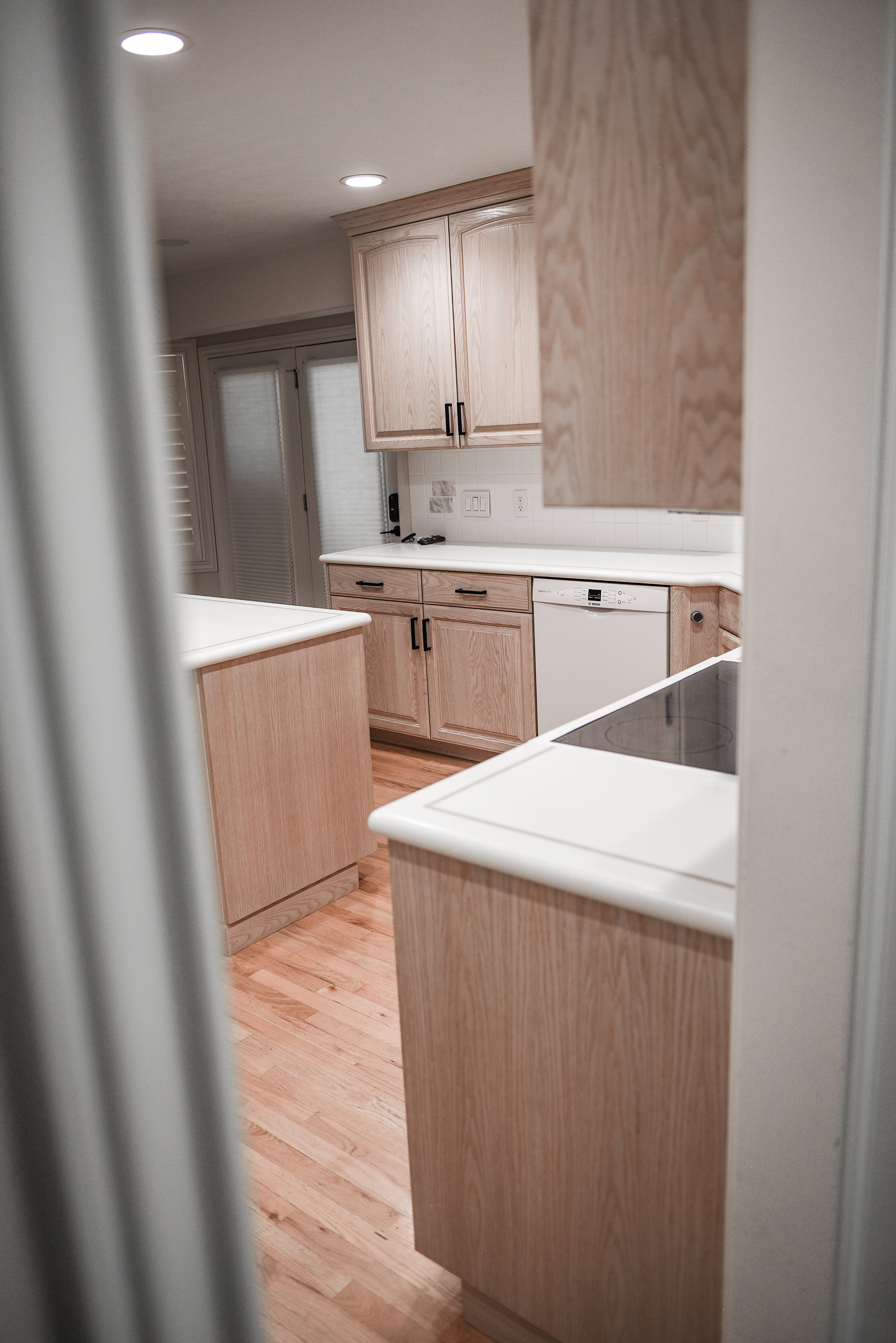 Kitchen featuring light wood-finish cabinetry with dark hardware, white countertops, built-in dishwasher, and recessed lighting