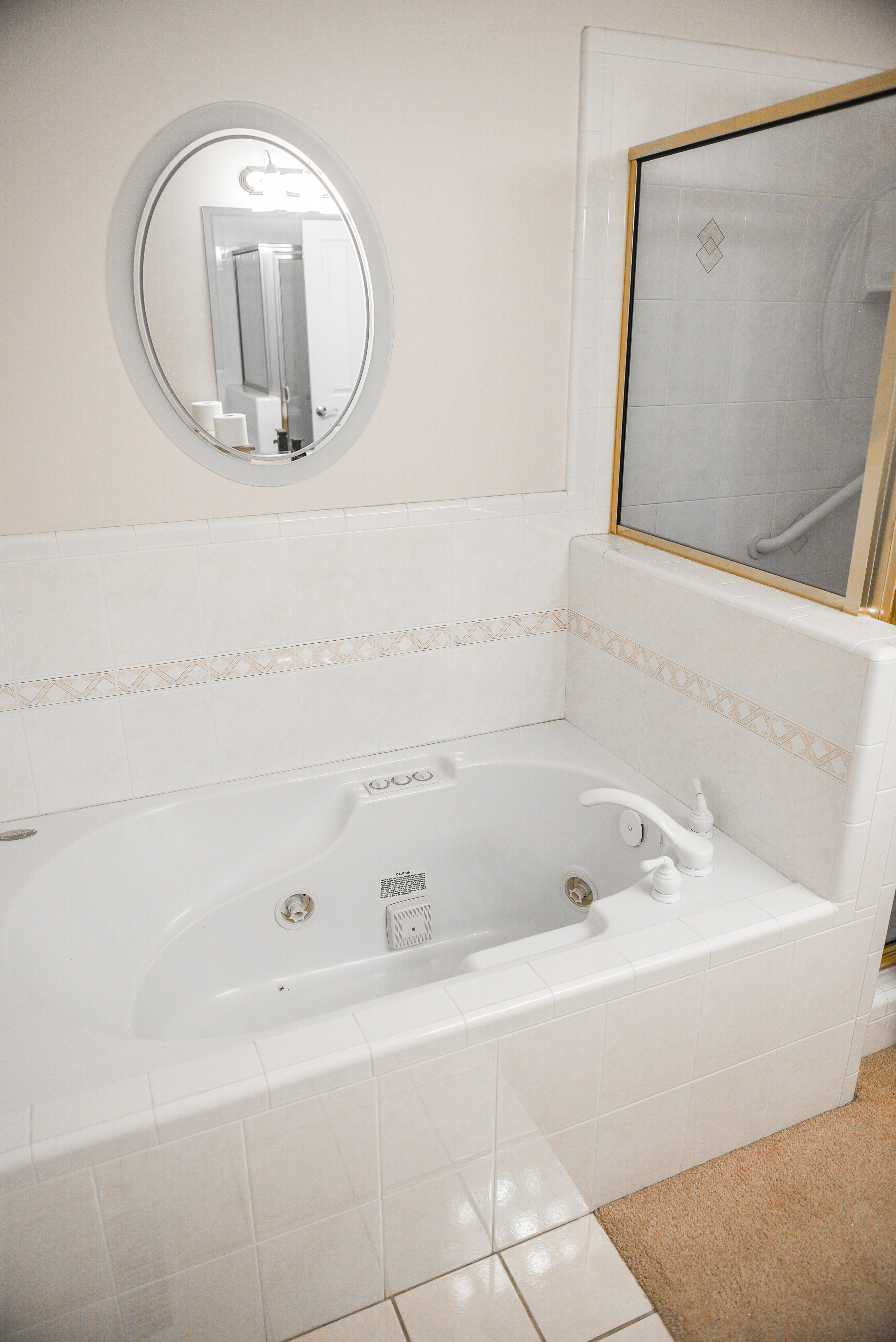 Soaking tub with white tile surround featuring decorative accent tile and a wall-mounted oval mirror