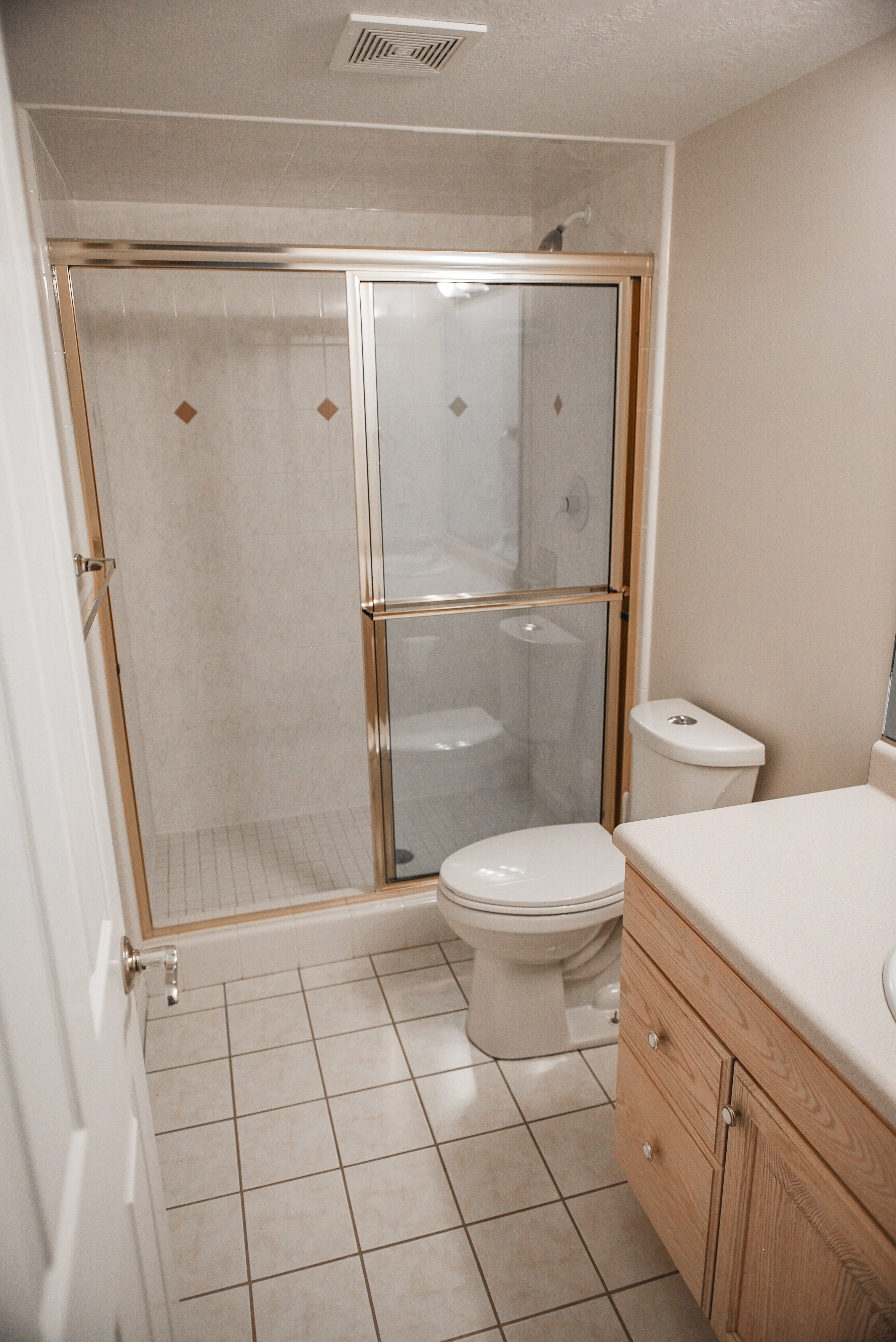 Bathroom featuring a shower with gold-toned framed glass doors, a single vanity with wood cabinetry, and square ceramic tile flooring