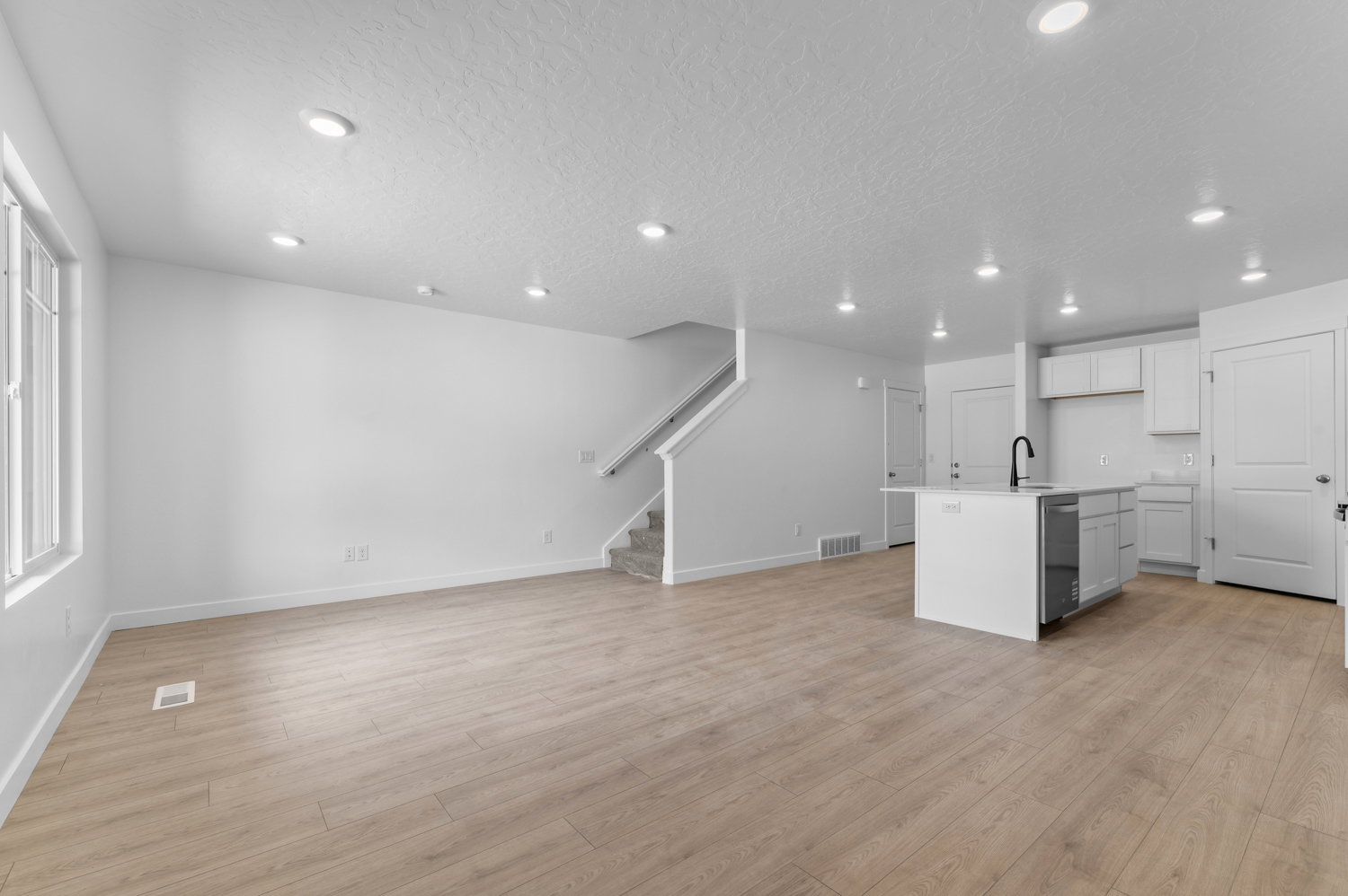 Open-concept living space featuring wood-finish flooring, recessed lighting, and a modern kitchen island with an integrated sink and black faucet