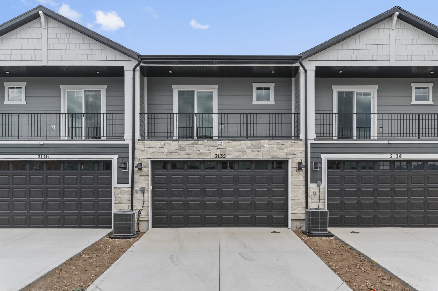 Modern townhouse exterior featuring gray siding, stone veneer accents, and dark garage doors