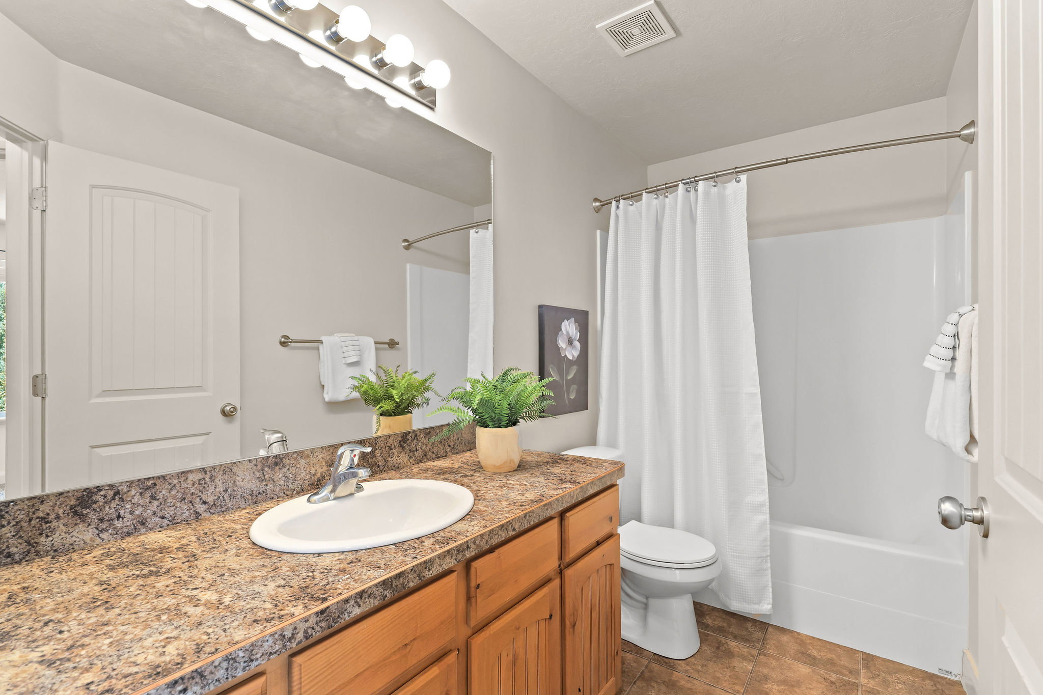 Bathroom featuring a wood-finish vanity with a built-in sink, a speckled countertop, a large wall mirror, and a full shower-tub combination with white surround