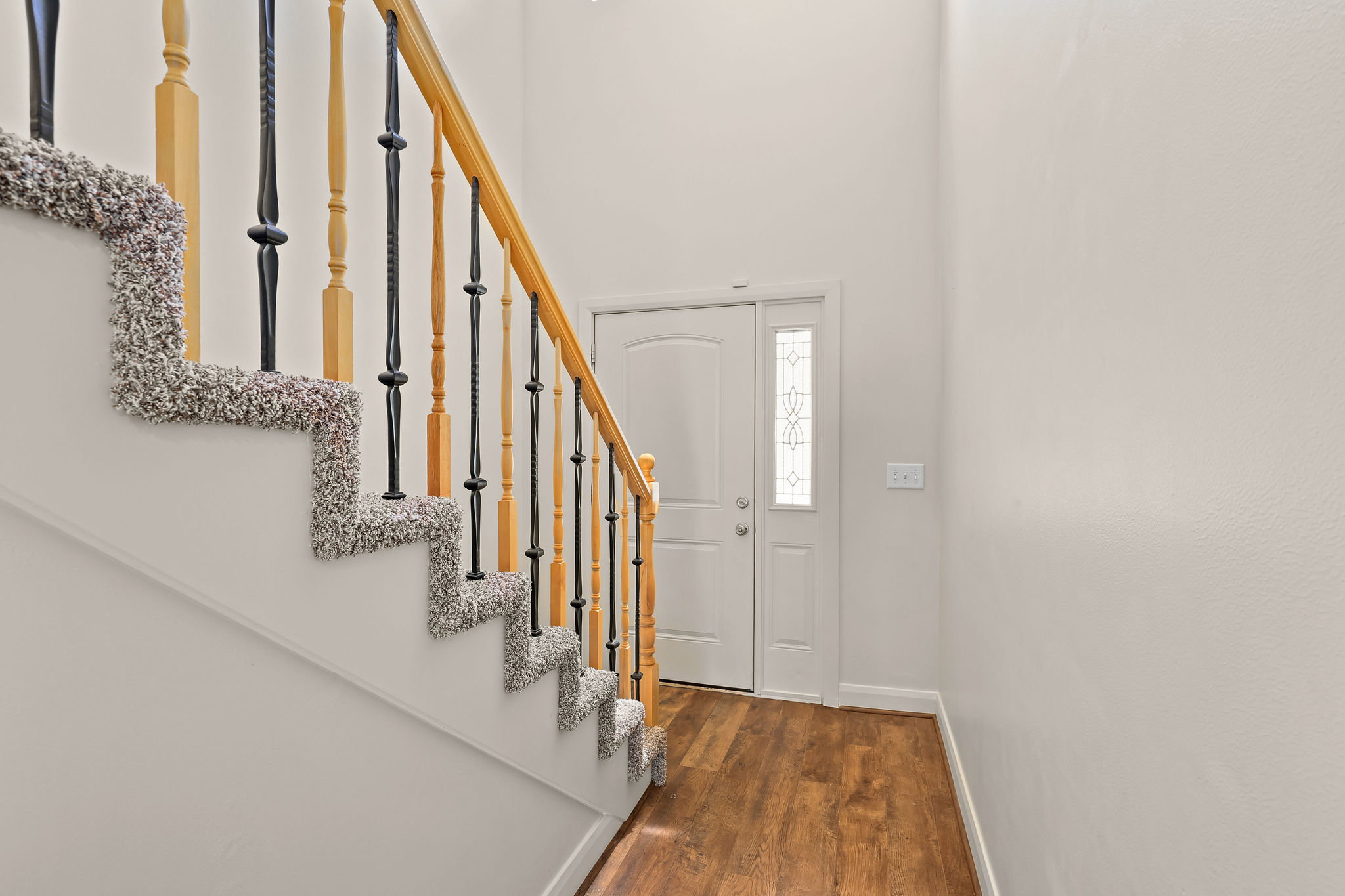 Entryway featuring wood-finish flooring, a white paneled door with a decorative glass sidelight, and a staircase with a light wood handrail, black metal balusters, and carpeted treads
