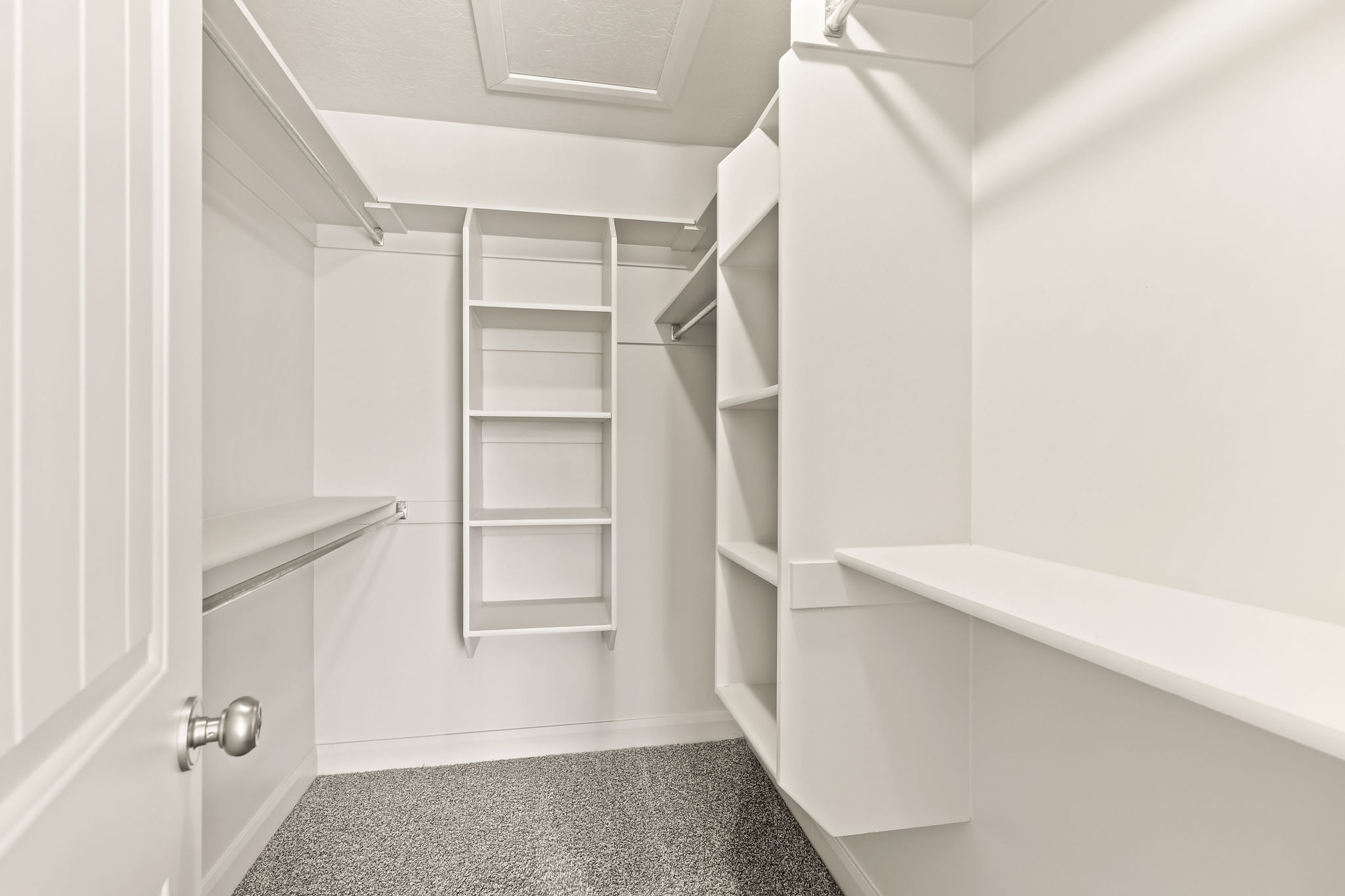 Walk-in closet featuring built-in shelving, hanging rods, an attic access panel, and neutral gray carpeting