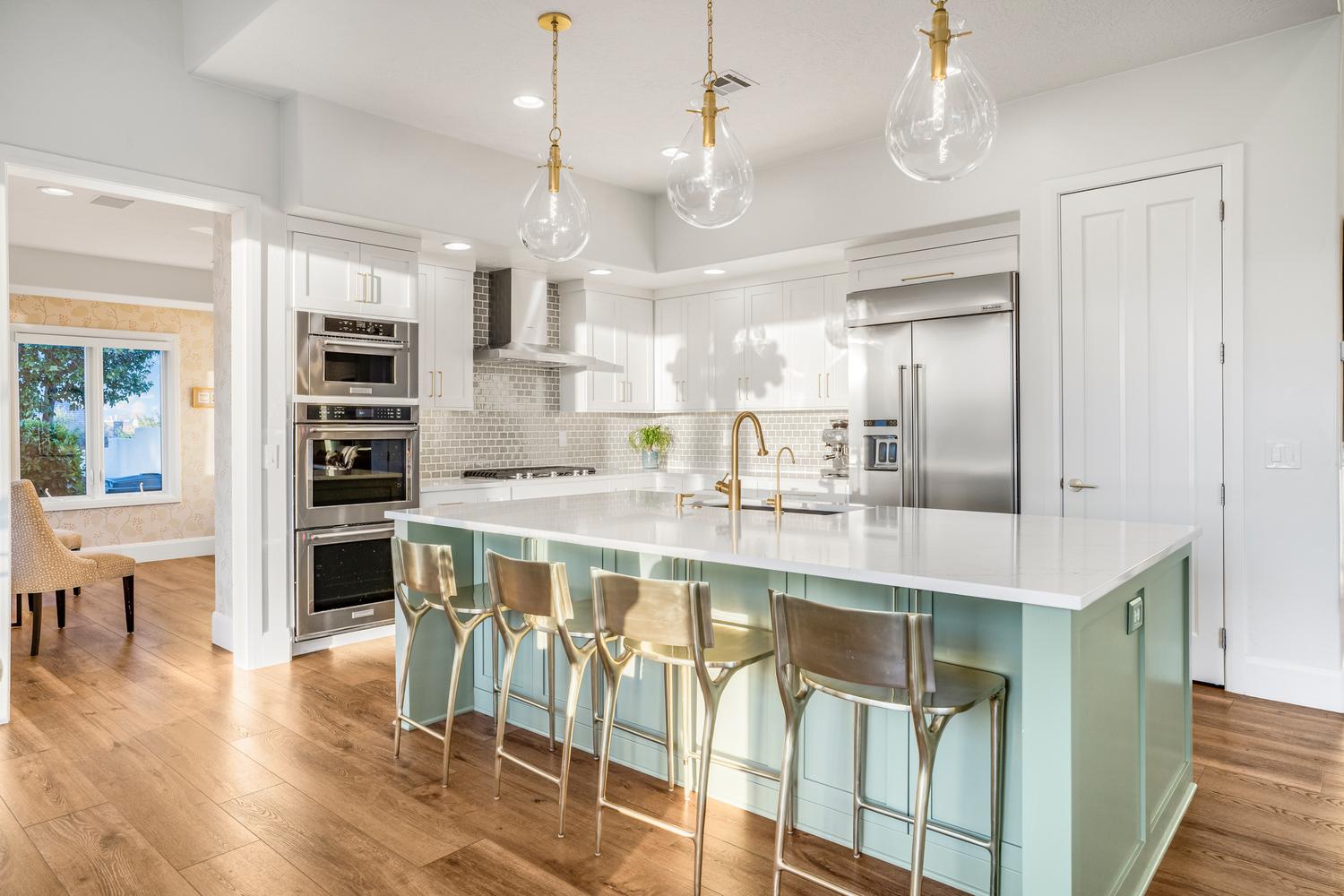 Contemporary kitchen featuring a light green island with a white countertop, gold-toned pendant lighting, stainless steel appliances, white cabinetry, and wood-finish flooring