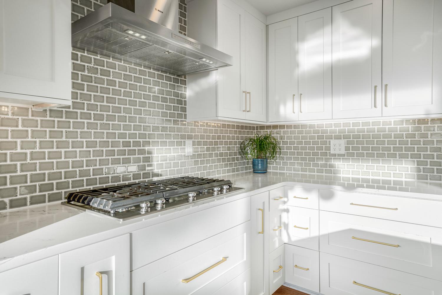 Kitchen featuring a gas range, stainless steel range hood, white cabinetry, light countertops, and a gray subway tile backsplash