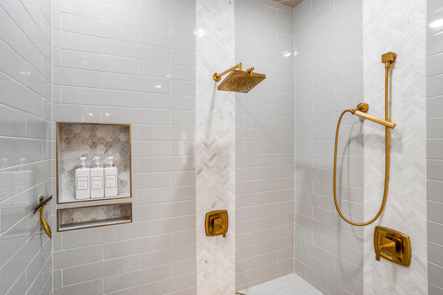 Shower enclosure featuring light gray subway tile walls and herringbone pattern accent tile