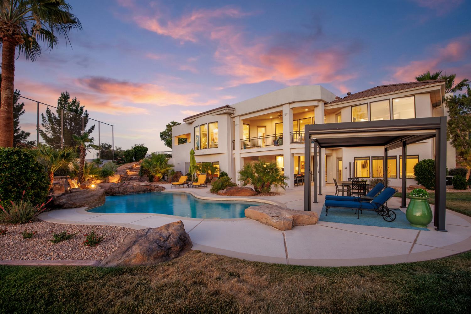 Expansive backyard featuring a large swimming pool with rock waterfall features, mature palm trees, and integrated landscape lighting
