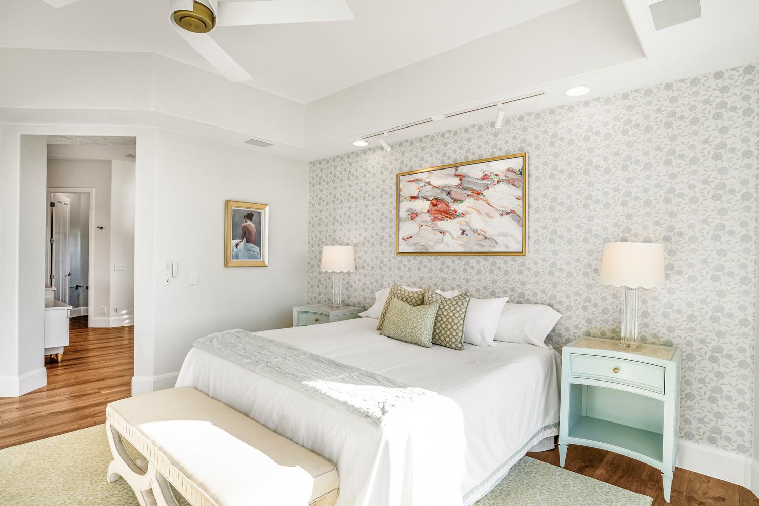 Bedroom featuring patterned accent wall, recessed ceiling with fan, track lighting, and wood-finish flooring