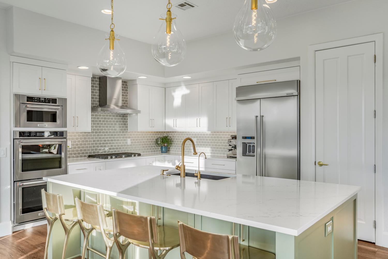 Contemporary kitchen featuring a large center island with a light-toned countertop, white cabinetry, integrated stainless steel appliances, a tile backsplash, and decorative pendant lighting