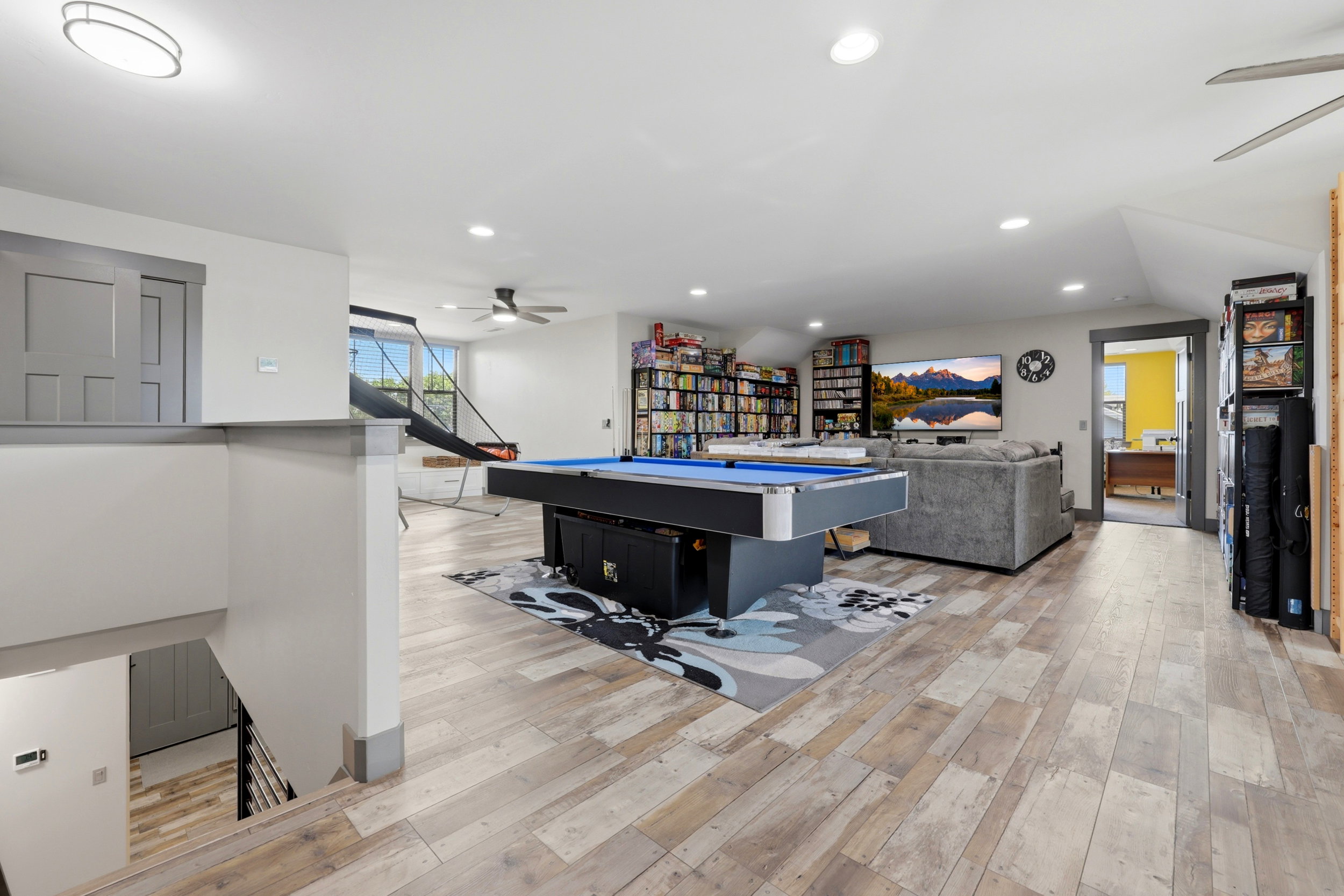 Spacious open-concept room featuring wood-finish flooring, recessed lighting, ceiling fans, and a built-in shelving unit