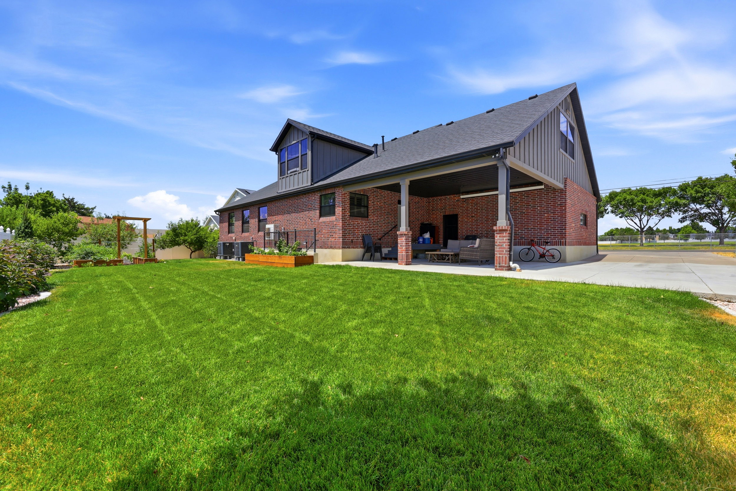 Expansive green lawn with a covered patio, brick exterior, and a dormer window