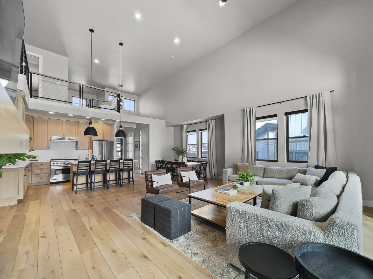 Open-concept living space featuring wood-finish flooring, a kitchen island with seating, stainless steel appliances, and a second-story interior balcony