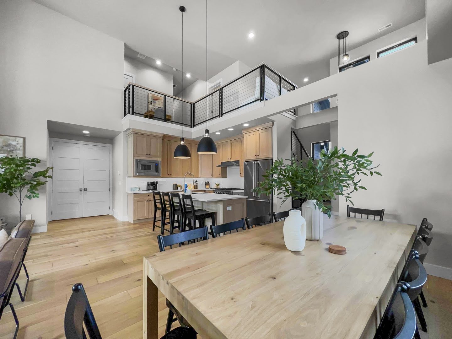 Open concept living space featuring a gourmet kitchen, light wood-finish flooring, and a second-story interior balcony with horizontal metal railings