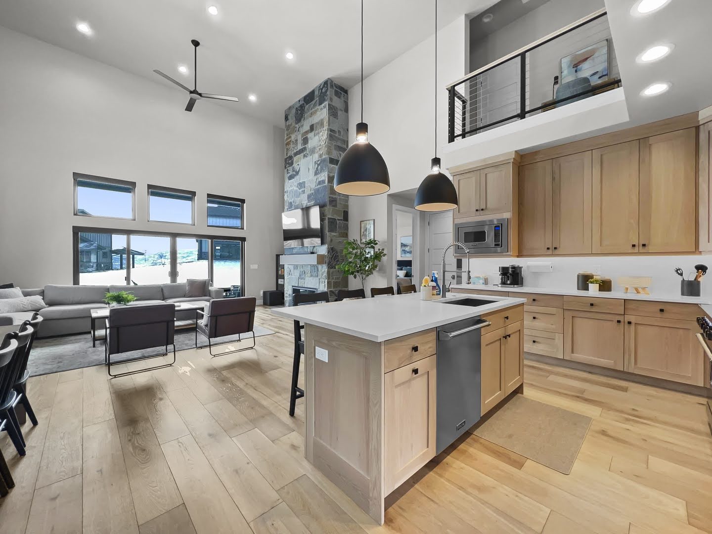 Open-concept living space featuring high ceilings, wood-finish flooring, a stone-clad fireplace, and a kitchen island with pendant lighting