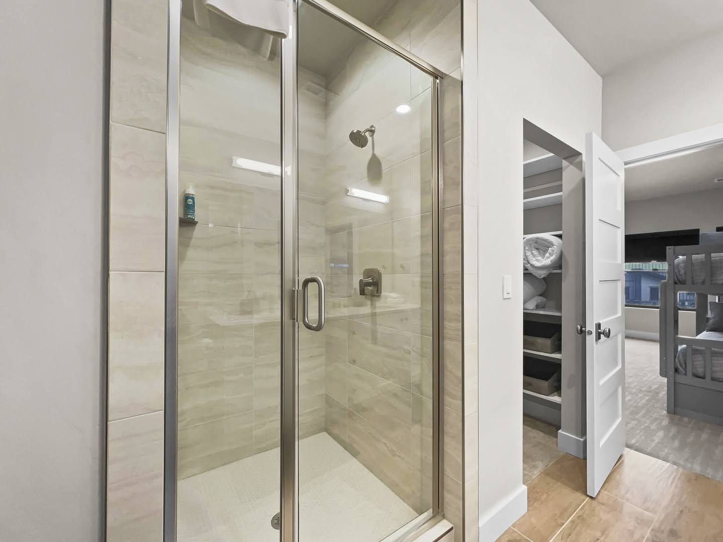 Glass-enclosed shower with tile surround and integrated shelving, featuring a mounted showerhead and a brushed nickel handle