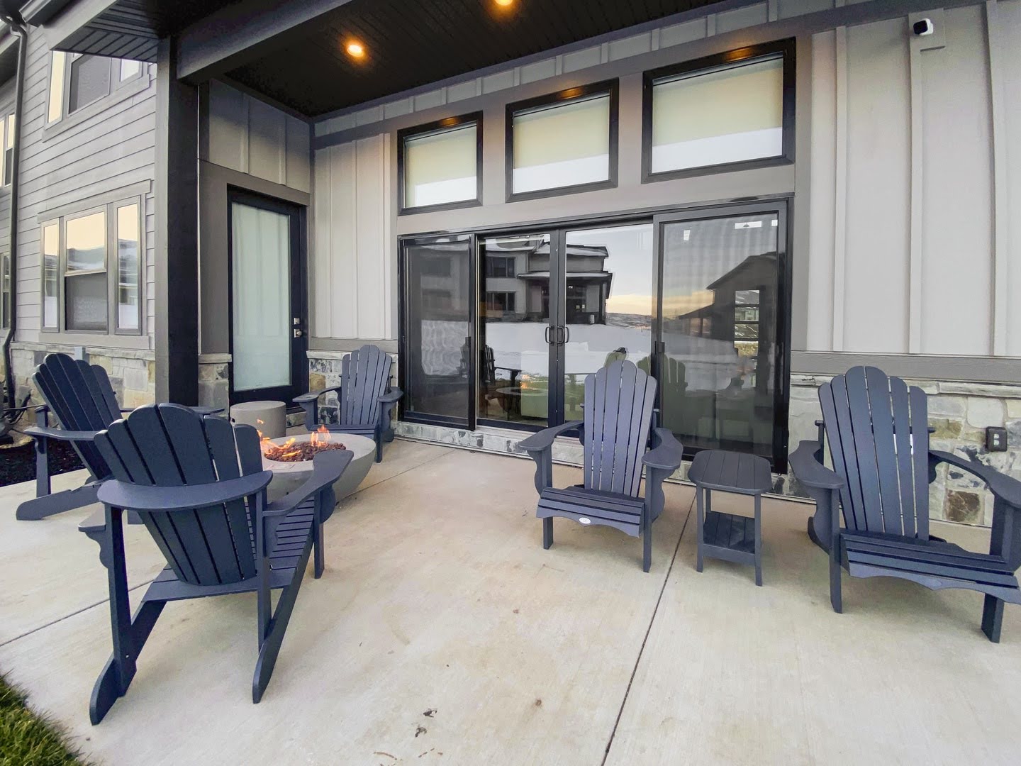 Expansive concrete patio with a modern fire pit, sliding glass doors, and recessed overhead lighting