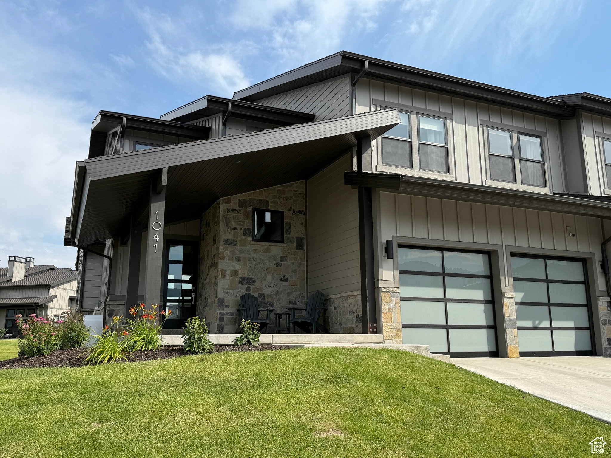 Modern exterior featuring vertical siding, stone accents, two contemporary garage doors, a covered entry, and landscaped plantings