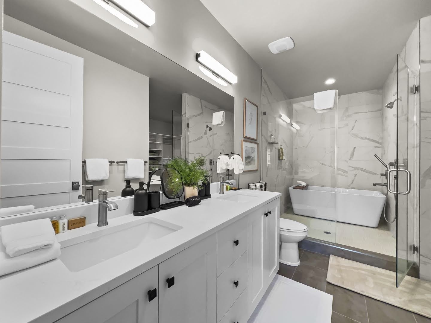 Contemporary bathroom featuring a double vanity with integrated sinks and black hardware, a freestanding soaking tub, a glass-enclosed shower, and large-format tile flooring