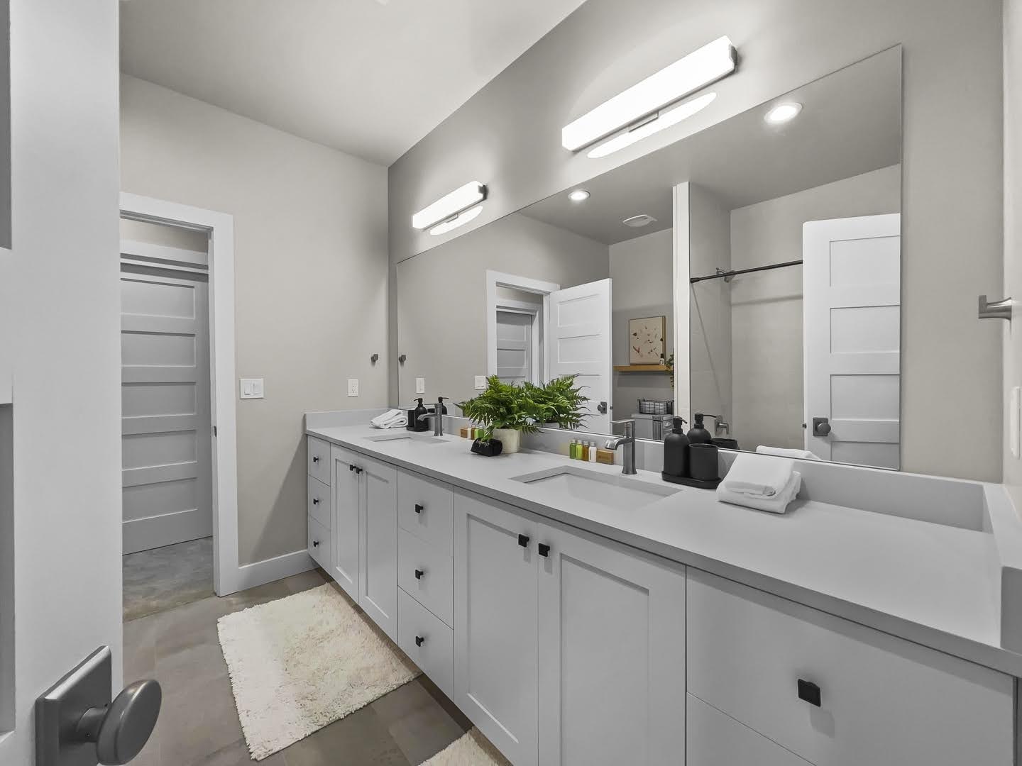 Spacious bathroom featuring a dual vanity with light gray cabinetry, integrated sinks, a large wall-mounted mirror, and matte black hardware
