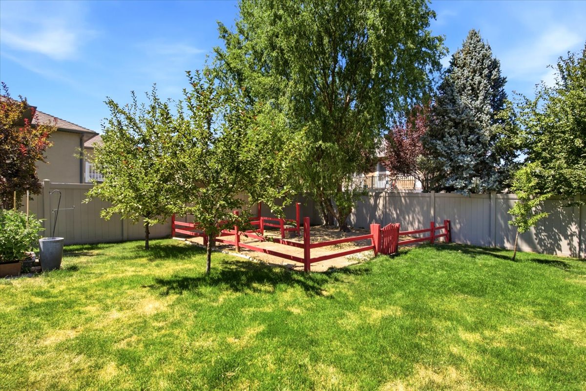 Expansive backyard featuring a lush lawn, mature trees, a perimeter fence, and a red decorative fence feature