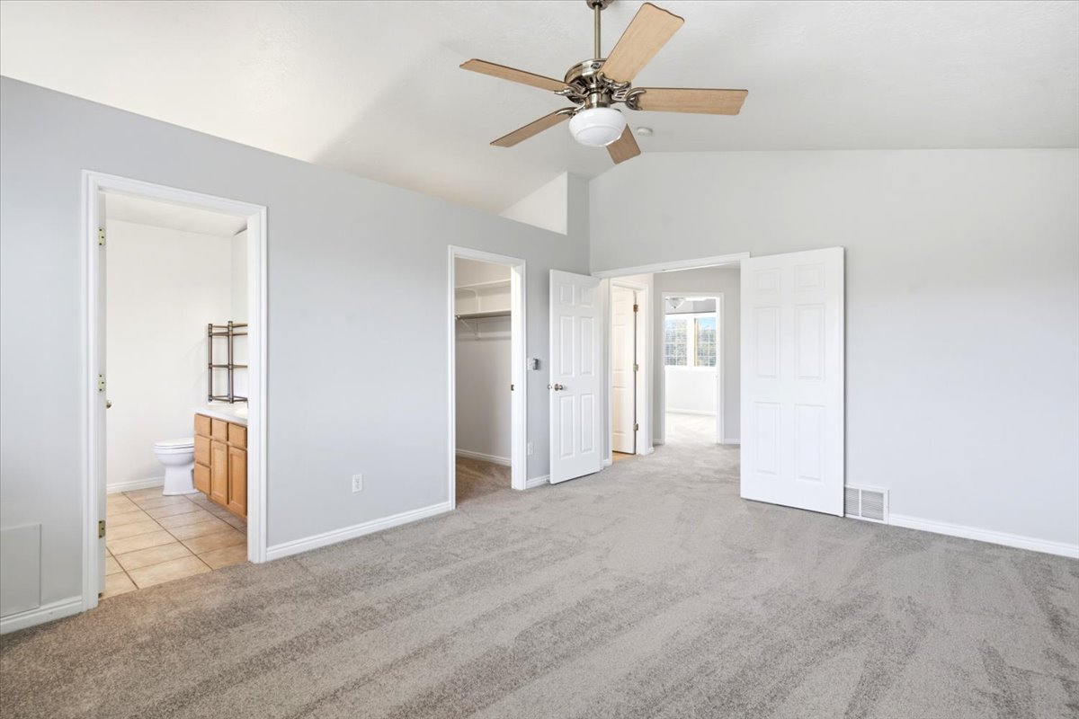 Carpeted room with vaulted ceilings and a ceiling fan