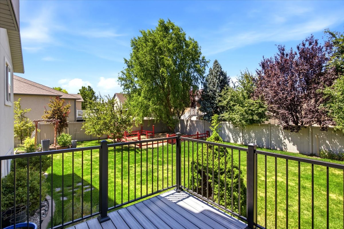 Upper-level deck featuring composite wood-finish decking and black metal railings, overlooking a spacious lawn