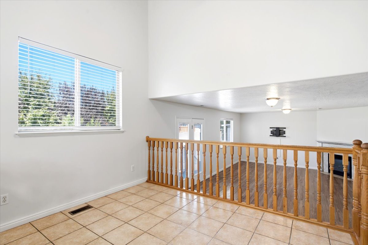 Upper-level landing featuring ceramic tile flooring, a natural wood balustrade, and a prominent window with horizontal blinds