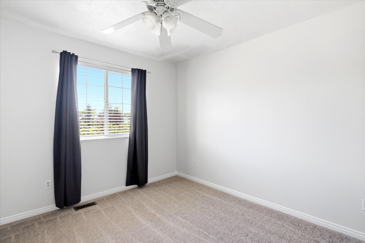 Bright room featuring a large window with horizontal blinds, neutral carpeting, white baseboards, and a ceiling fan with integrated lighting