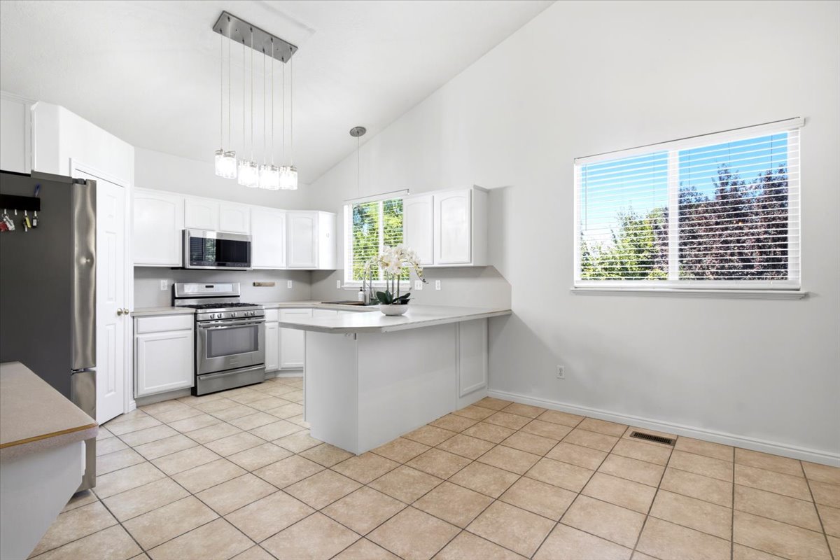 Bright kitchen featuring vaulted ceilings, white cabinetry, stainless steel appliances, a breakfast bar, and tile flooring