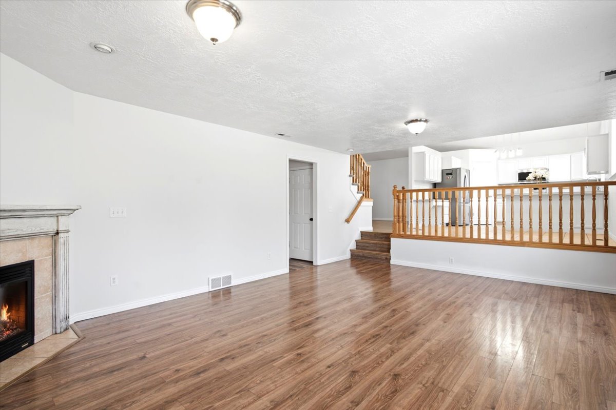 Spacious room featuring wood-finish flooring, a corner fireplace with a stone surround and mantel, and white walls