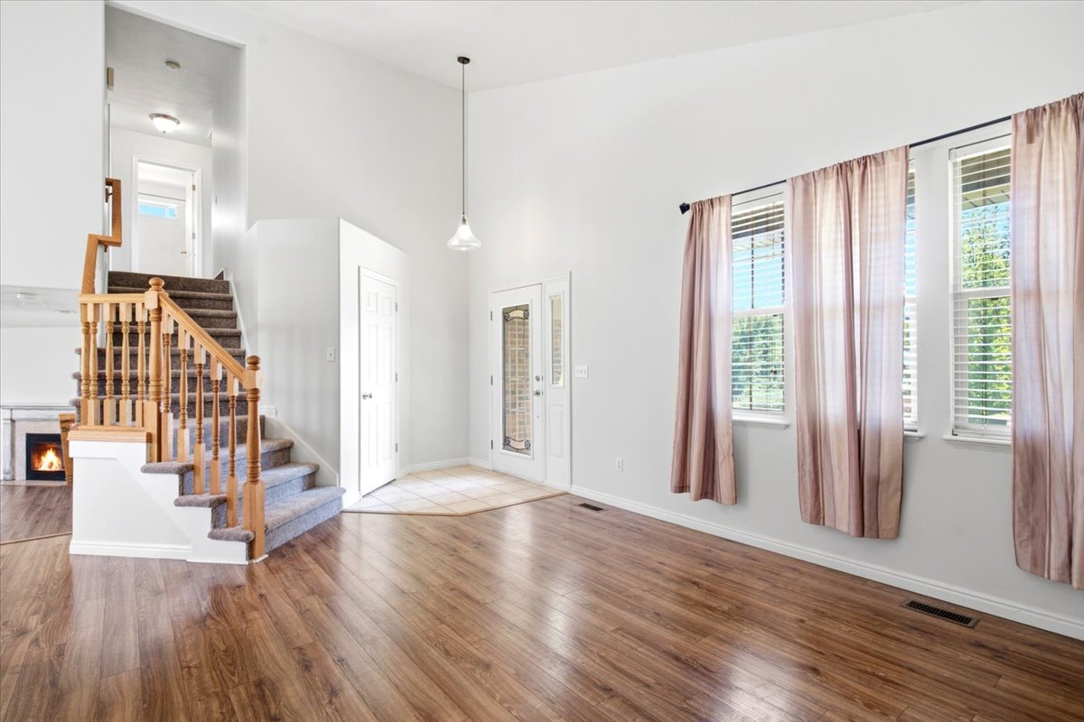 Spacious living area featuring high ceilings, wood-finish flooring, a contemporary fireplace, and a grand staircase with wood banisters