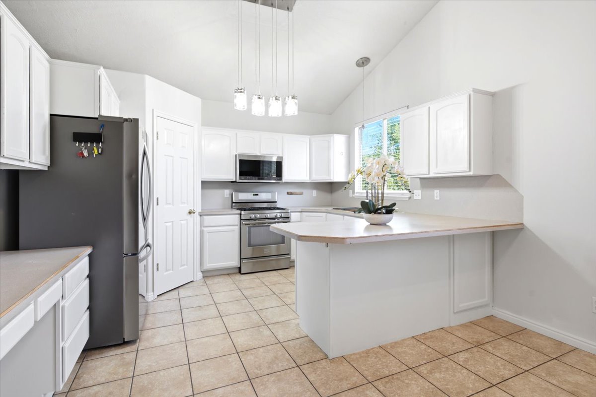 Kitchen featuring white cabinetry, stainless steel appliances, a breakfast bar, vaulted ceilings, and tile flooring