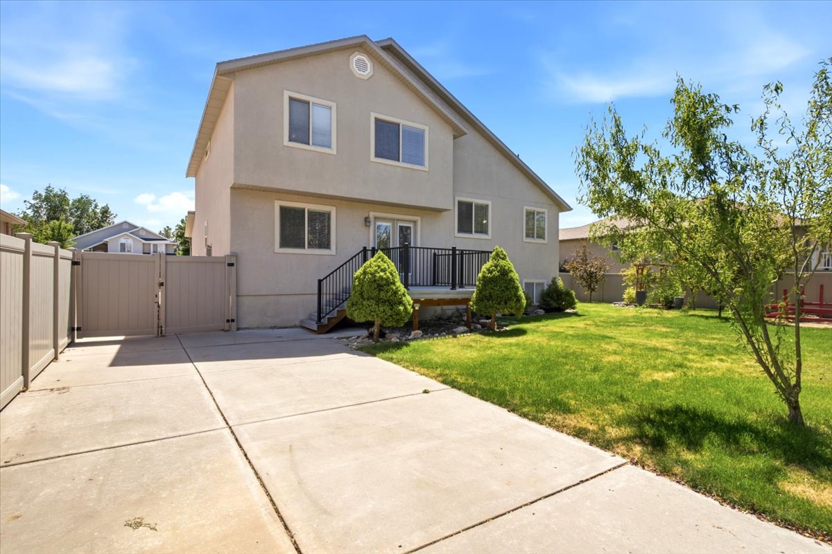 Rear exterior featuring a concrete driveway, fenced perimeter, and a grass lawn