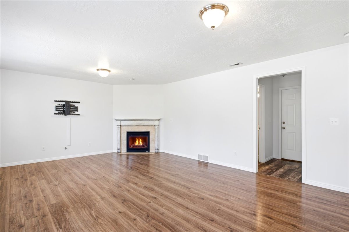 Spacious living area featuring wood-finish flooring, a corner fireplace with a stone surround, and an entry door