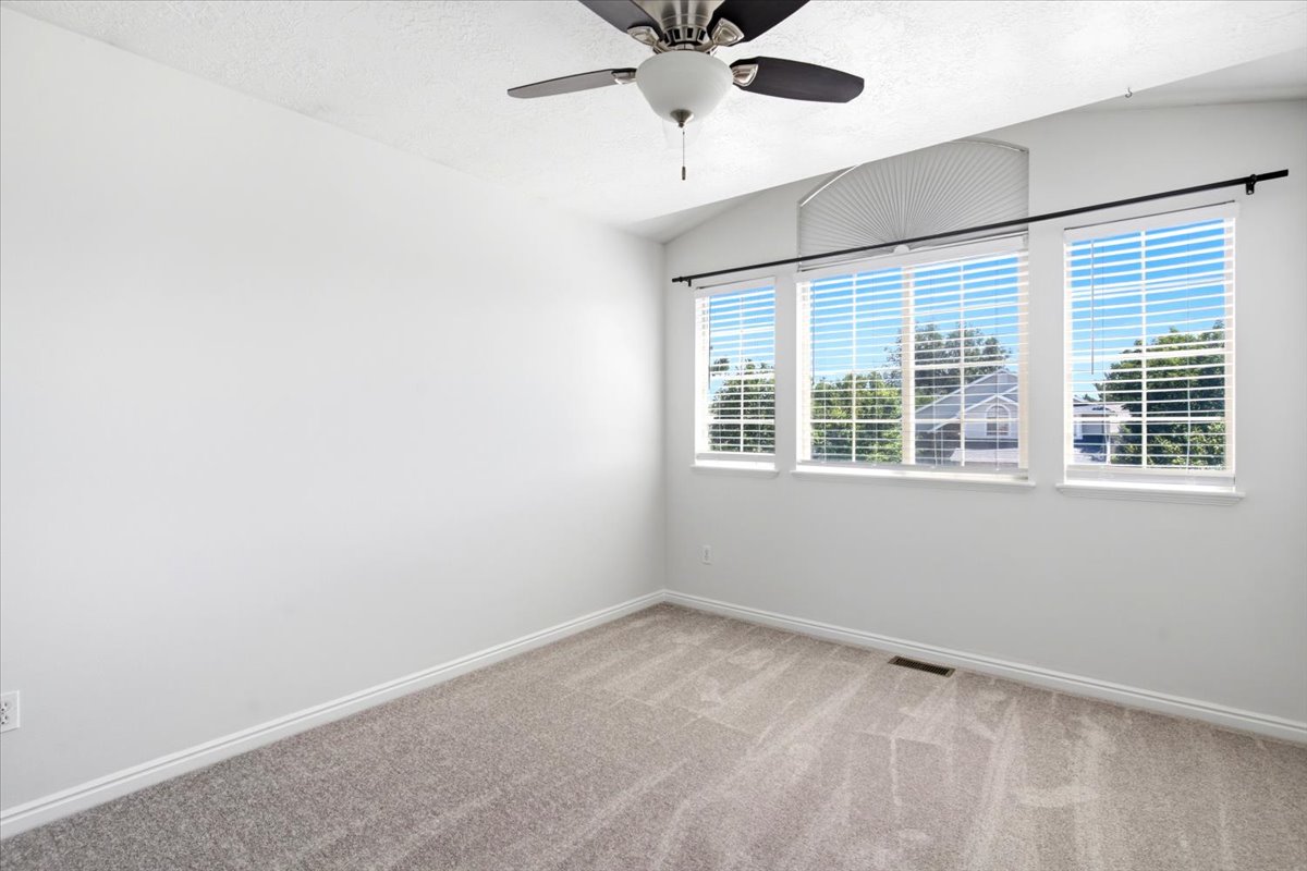 Room featuring neutral-toned carpet, white walls, and a vaulted ceiling with a ceiling fan