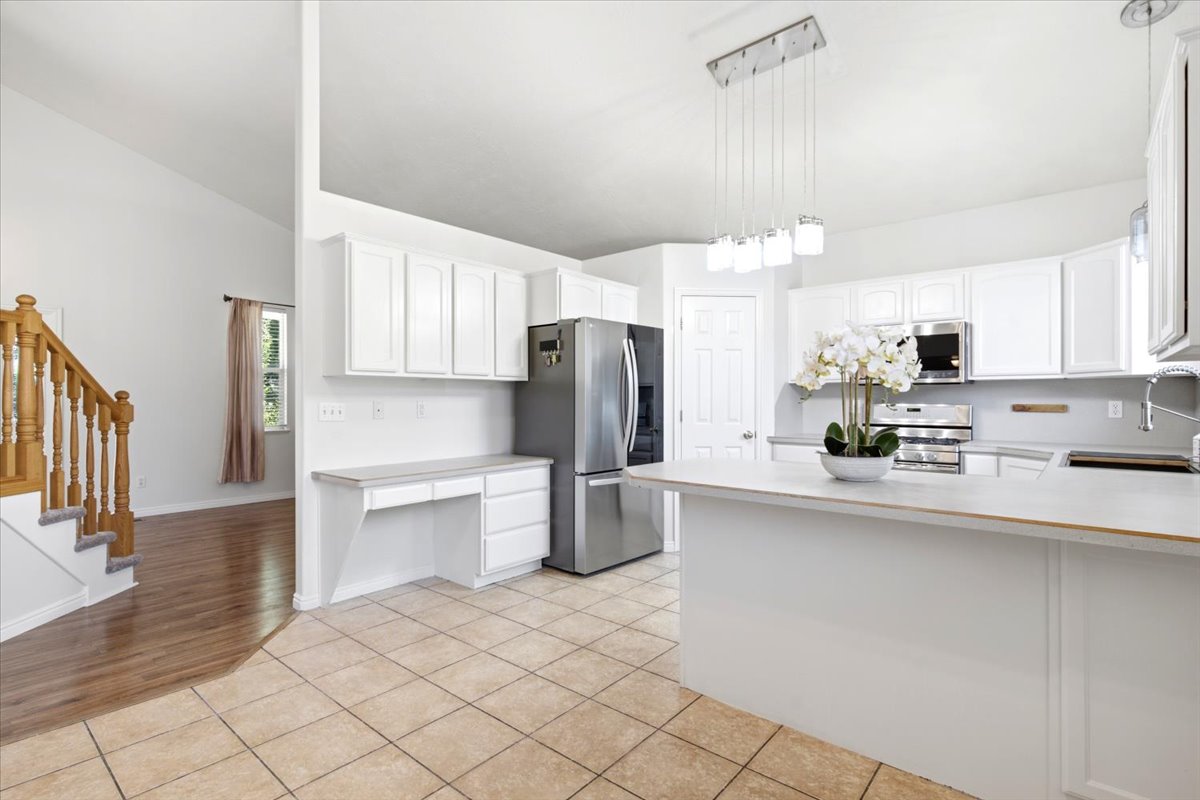 Kitchen featuring white cabinetry, stainless steel appliances, a center island with countertop seating, a built-in desk area, and tile flooring