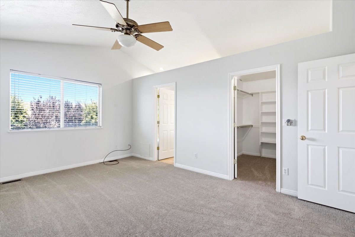 Spacious room featuring vaulted ceilings, light gray carpeting, and a large window with horizontal blinds
