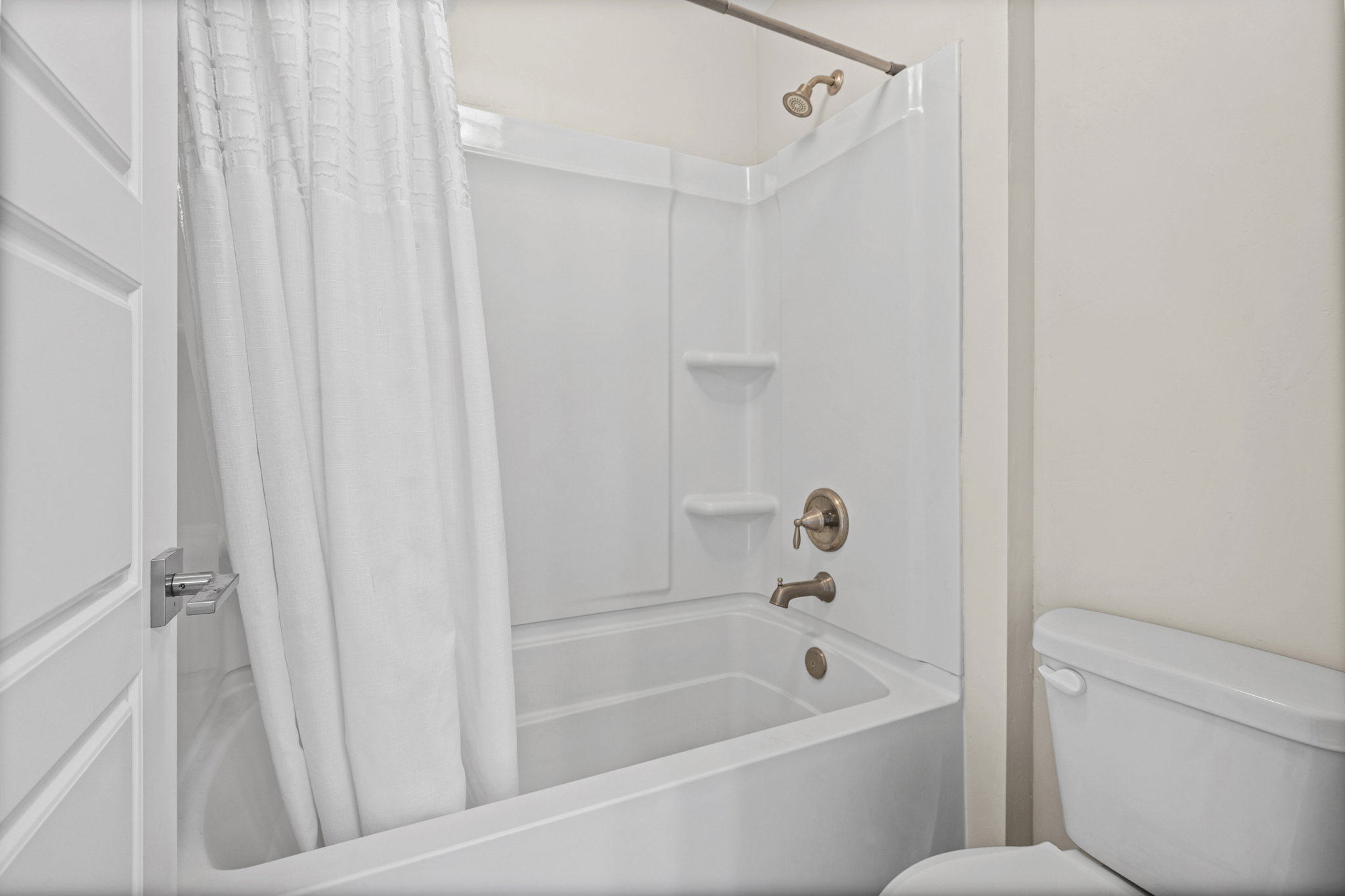 Bathtub and shower combination featuring brushed nickel fixtures and integrated shelving