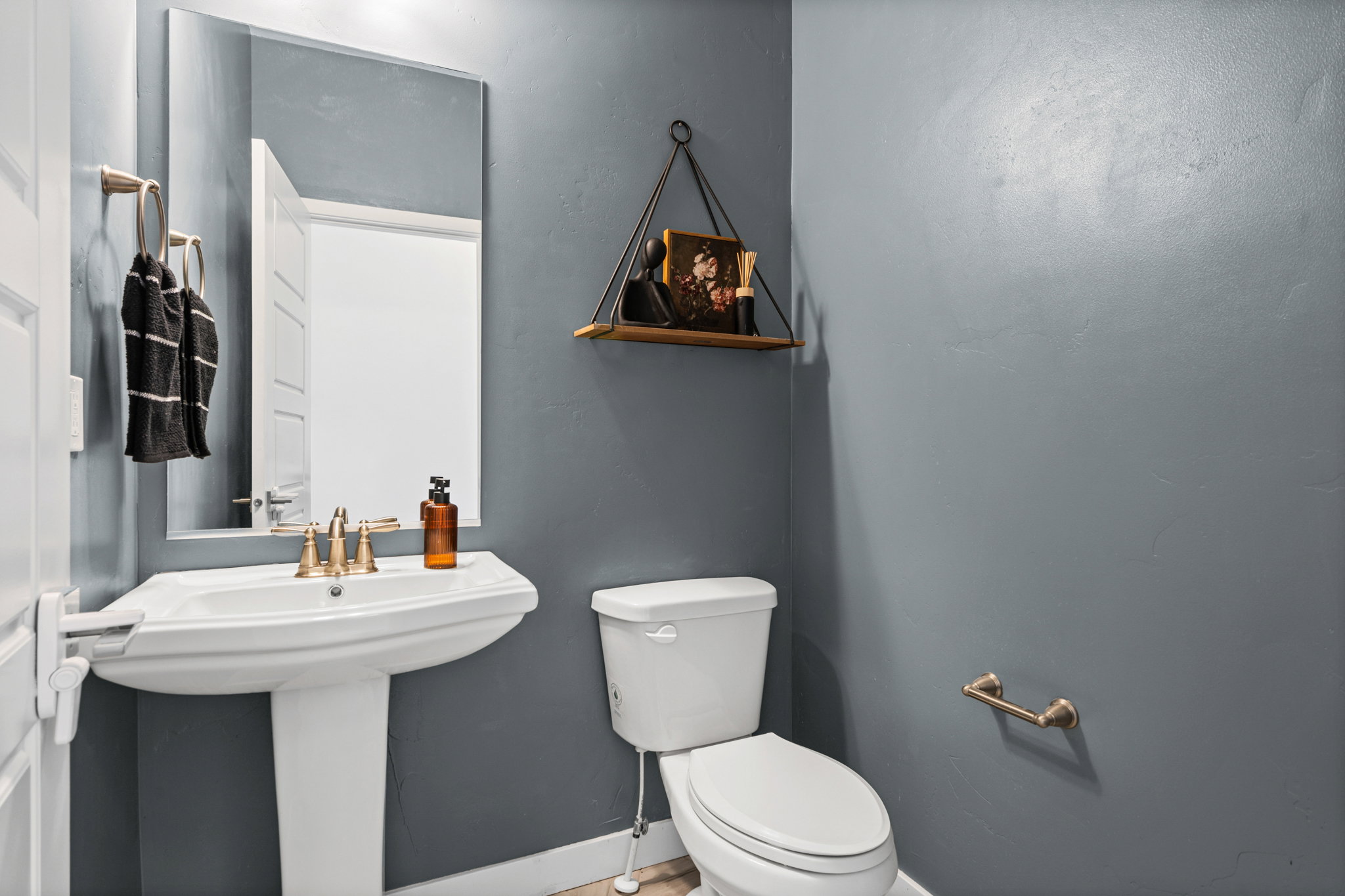 Pedestal sink with brass-finish faucet, toilet, wall-mounted mirror, and brass-finish towel ring