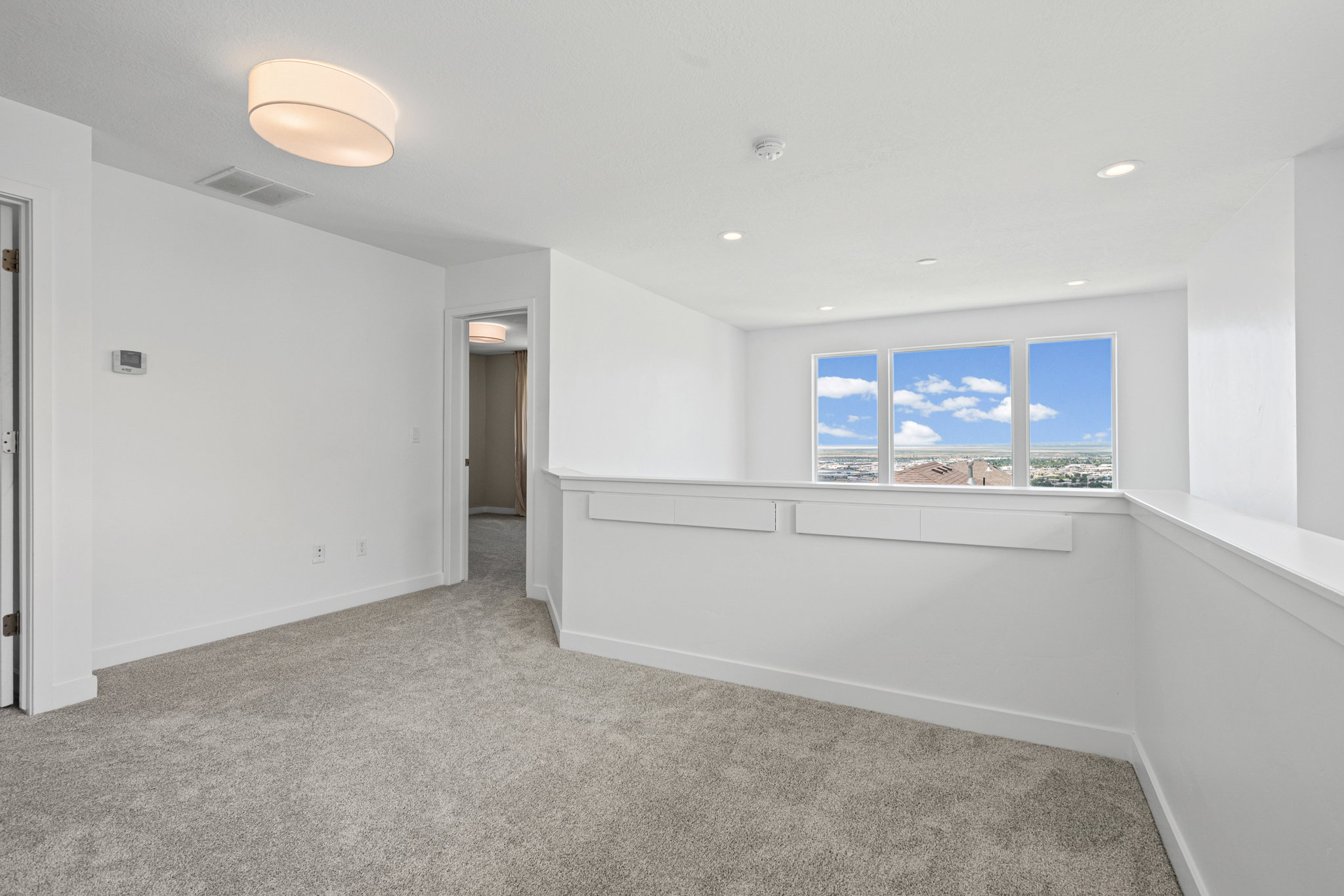 Carpeted upper-level landing featuring a half wall with integrated storage, a trio of large windows with white trim, and recessed ceiling lighting