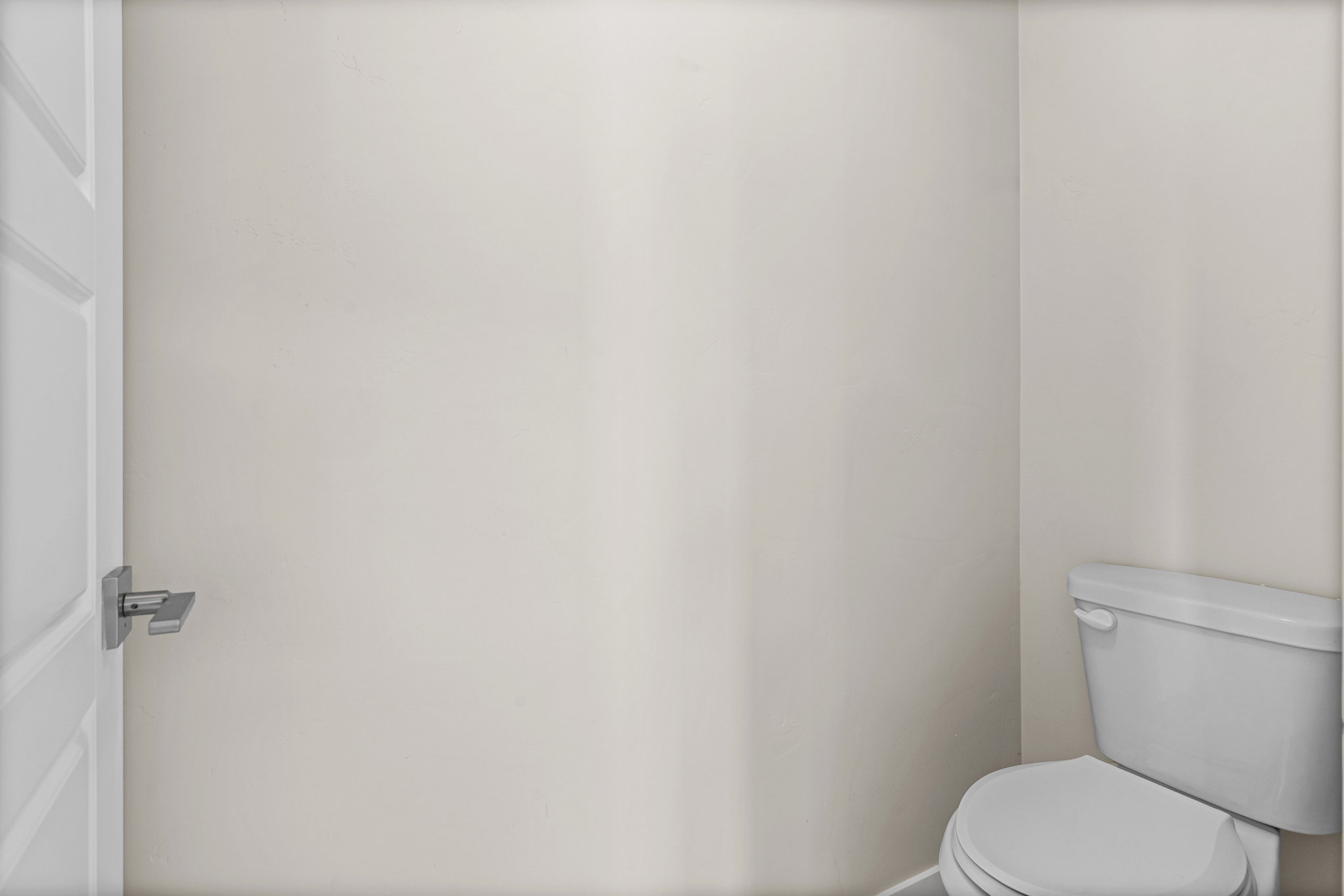Compact water closet featuring a modern white toilet, light-toned walls, and a white paneled door with a contemporary brushed nickel door handle
