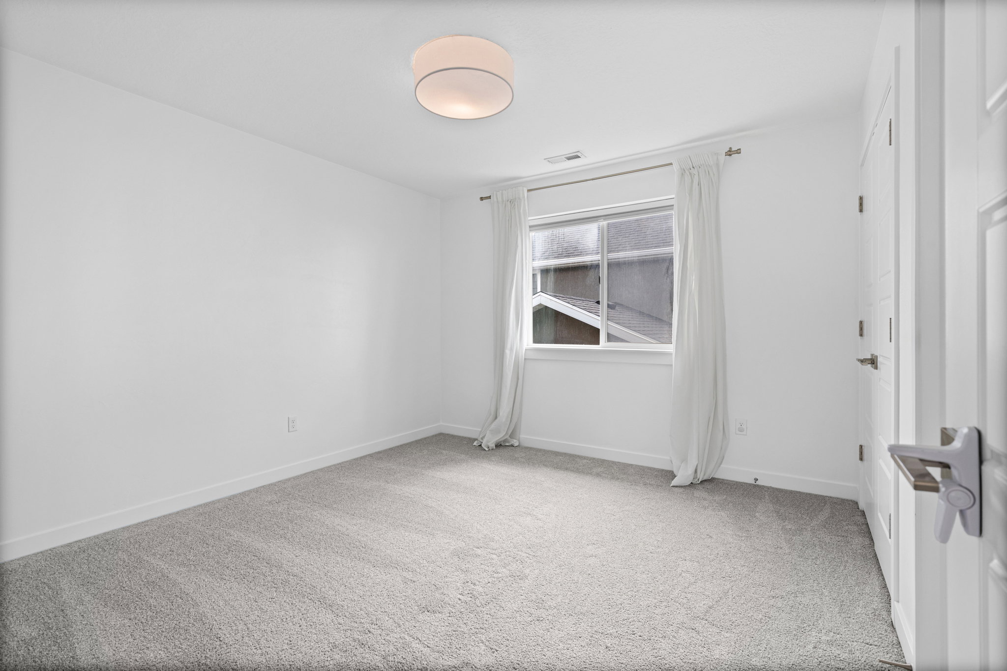 Spacious room featuring neutral carpeting, white walls, a double-hung window, and a contemporary flush-mount ceiling light fixture