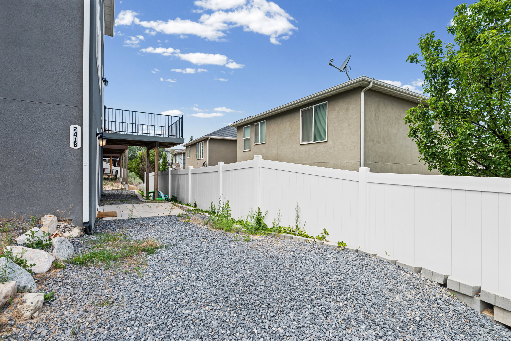 Gravel pathway leading to the property entrance, with a white privacy fence and a dark gray exterior